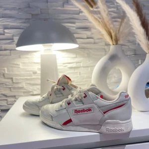 Vita Reebok sneakers med röda detaljer - Säljer ett par klassiska vita Reebok sneakers med snygga detaljer. Skorna har snörning och är i bra skick, perfekta för vardagsbruk. De är bekväma och stilrena, passar till det mesta i garderoben. Perfekta för dig som gillar en sportig look!
