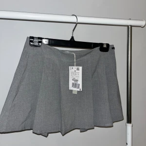 Grå kjol från Pacific Republic - Snygg grå kjol från Pacific Republic i en kort modell. Kjolen har en klassisk design med en lätt utställd form som ger en fin siluett. Perfekt för att matcha med olika toppar och accessoarer.