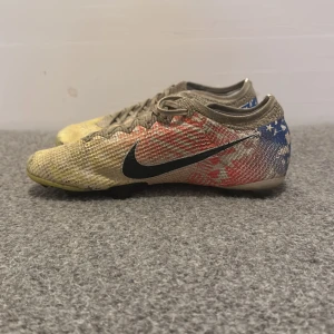 Nike fotbollsskor Neymar special edition  - Snygga Nike fotbollsskor med ett unikt mönster i beige, blått och rött. Skorna har snörning och är perfekta för fotbollsspel på gräs. De har en slitstark sula med dobbar för bra grepp. Mitt pris 149 nytt pris 1899