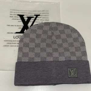 Grå rutig mössa från Louis Vuitton - Snygg grå rutig mössa från Louis Vuitton i ett mjukt och bekvämt material. Den har en klassisk design med ett diskret LV-märke framtill. Perfekt för att hålla sig varm med stil under kyliga dagar.