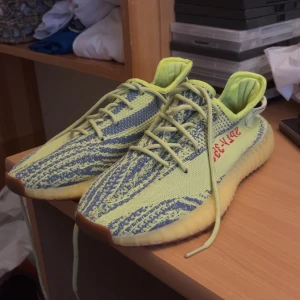 Adidas Yeezy Boost 350 V2 i gul och grön - Säljer ett par Adidas Yeezy Boost 350 V2 i en cool gul och grön färgkombination. Skorna har en stickad ovandel med snörning och en bekväm, dämpad sula. Perfekta för både vardag och fest! De är i mycket bra skick och redo för en ny ägare.