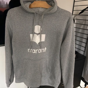 Grå hoodie från Marant - Säljer en snygg grå hoodie från Marant i mycket bra skick. Den har en klassisk passform med en stor logga framtill och praktisk magficka. Perfekt för höst och vinter, och den är supermjuk och bekväm. Passar både till vardags och chillkvällar. 🩶