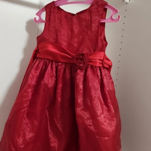Röd glittrig klänning för 5-7år - Säljer en superfin röd klänning i glittrigt material. Den är ärmlös och har en söt rosett i midjan. Perfekt för festliga tillfällen! Klänningen har en knäppning bak och är i mycket bra skick. Passar 5-7år