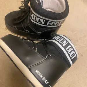 Säljer ett par svarta Moon Boots. De har en cool design med snörning och en bred vit rand med loggan runt skaftet. Perfekta för vintern då det varma och bekväma🥰