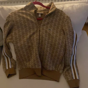 Lacoste MONOGRAM - Säljer en monogram från Lacoste i mycket bra skick. Den har långa ärmar med vita och blå ränder längs sidorna och en dragkedja framtill. Perfekt för höst och vår! Ny pris 2.100