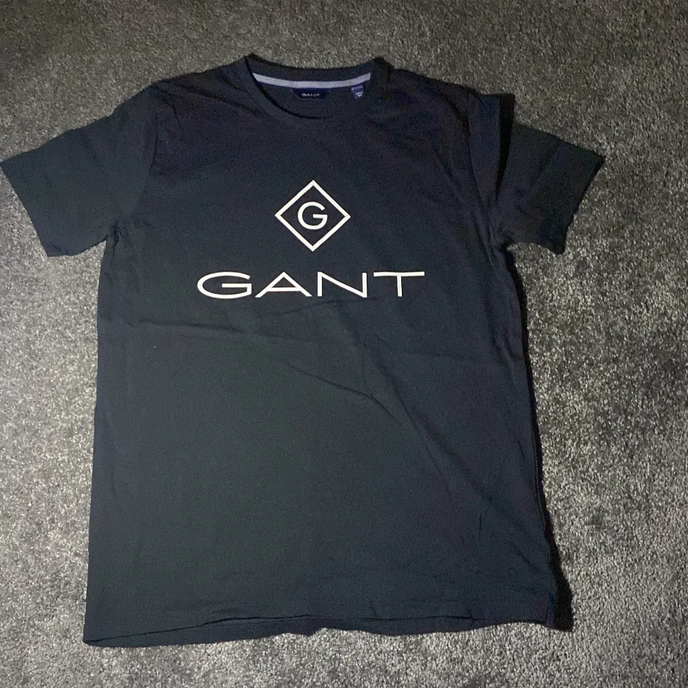 Säljer en till HELT NY snygg svart t-shirt från GANT i storlek 158/164 cm, perfekt för tonåringar. T-shirten har en stor vit logga på framsidan och är i mycket bra skick. Den är kortärmad och gjord av mjukt bomullsmaterial. Passar perfekt till både vardag och fest! Köpt på kidsbrandstore . T-paidat.