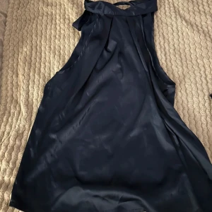 Marinblå ärmlös blus - Elegant marinblå ärmlös blus i ett glansigt material. Perfekt för en stilren look med en hög halsringning och en lös passform. 