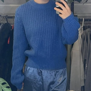 Blå stickad tröja - Säljer en snygg blå stickad tröja med rund hals och långa ärmar. Perfekt för kyligare dagar och ger en stilren look. Tröjan har en ribbad kant vid ärmslut och nederkant. 