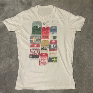 Vit t-shirt med färgglatt tryck dsquared2 - Snygg vit t-shirt med ett coolt, färgglatt tryck av olika etiketter och logotyper. Perfekt för en avslappnad stil. 