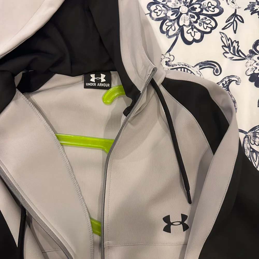 Säljer en snygg grå och svart hoodie från Under Armour. Den har en dragkedja framtill och en justerbar huva med snören. Perfekt för träning eller vardagsbruk. Den är i mycket bra skick och superbekväm!. Tröjor & Koftor.