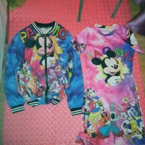 Färgglad bomberjacka med Disney-motiv - Säljer en färgglad bomberjacka med Disney-motiv o klänning.. Jackan har en dragkedja framtill och långa ärmar. Den är dekorerad med karaktärer som Musse Pigg och andra Disney-figurer i en livlig färgpalett av blått, rosa och gult.