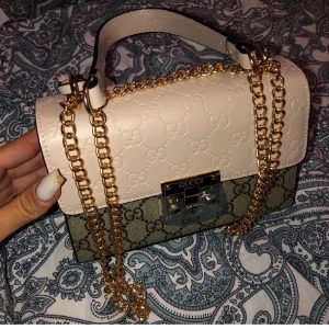 Gucci handväska med kedja - Säljer en superfin ny Gucci handväska. Väskan är i beige och brun med det klassiska Gucci-mönstret. Den har en elegant guldkedja och ett snyggt lås. Perfekt för både vardag och fest!