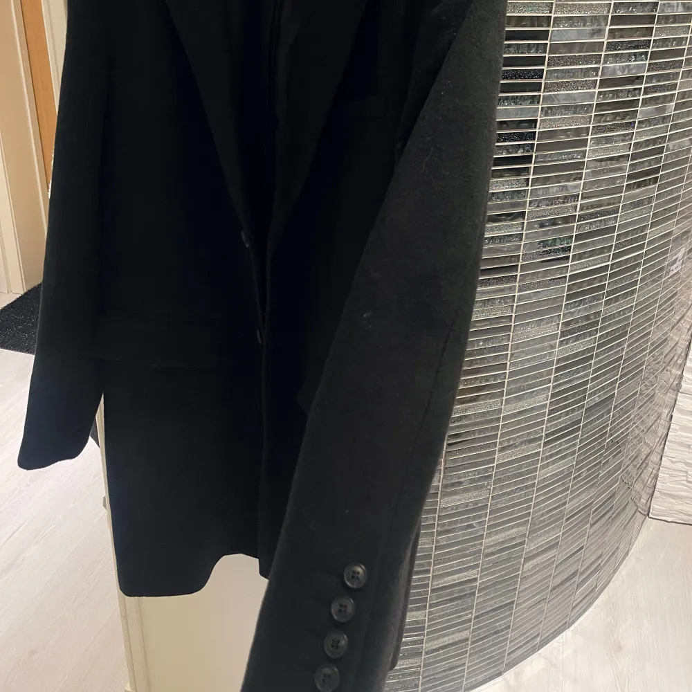 Säljer en stilren svart kappa i bra skick. Den har en klassisk design med knappar framtill och långa ärmar. Perfekt för höst och vinter, och funkar både till vardags och fest. Passar bra över en tröja eller skjorta för en elegant look. S/M storlek. Takit.