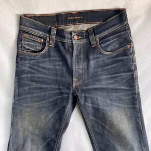Mörkblå jeans från Nudie Jeans - Säljer ett par snygga mörkblå jeans från Nudie Jeans i storlek 30/34 men är uppsydda till 30/32. De har en klassisk femficksdesign med orange sömmar och en bekväm passform. Perfekta för både vardag och fest! 🕺Org pris 1300/mitt pris 499. Dom är aldrig använda därför är det Inge fel med dom.😀