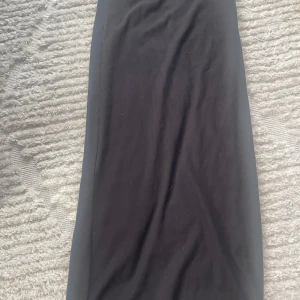 Svart ribbad Kjol - Säljer en svart ribbad kjol från Divided i storlek XXS. Perfekt för både vardag och fest! Klänningen är i nyskick och har en tight passform som framhäver figuren. Den är ärmlös och har en stilren design som gör den lätt att matcha med olika accessoarer.