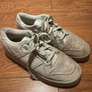 Mintgröna sneakers från Adidas i mocka - Säljer ett par snygga mintgröna sneakers från Adidas. De är i mocka och har en klassisk design med snörning. Perfekta för vardagsbruk och ger en stilren look. Skorna är i använt skick men fortfarande bekväma och funktionella. Jag har inte mockarengöring hemma, så de säljs som de är. Se bilder. Storlek 41 1/2.