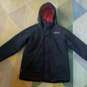 Svart vinterjacka eller skidjacka från Burton - Säljer en svart vinterjacka från Burton i mycket bra skick. Jackan har en röd insida som på bilden. Inga skador. Passar barn 10-12 år
