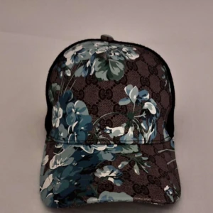 Gucci keps - Snygg keps med blommigt mönster och monogramdesign. Perfekt för att ge din outfit en unik touch. Justerbar passform och ventilerande mesh på baksidan.
