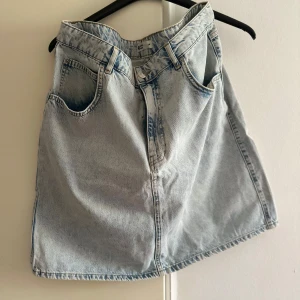 Ljusblå jeanskjol - Säljer en snygg ljusblå jeanskjol i klassisk stil. Kjolen har en normal passform och är perfekt för sommardagar. Den har praktiska fickor fram och en bekväm midja. Perfekt att matcha med en t-shirt eller blus för en avslappnad look.