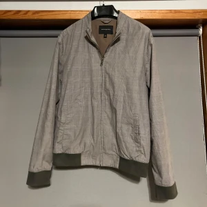 Grå rutig jacka från Banana Republic - Säljer en stilren grå rutig jacka från Banana Republic. Den har en dragkedja framtill och muddar vid ärmslut och nederkant. Perfekt för höst och vår med sin lätta och bekväma passform. Jackan är i mycket bra skick och redo för nya äventyr!