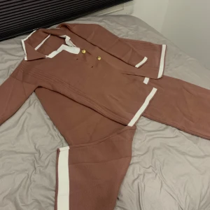 Sett/Overall - Säljer ett snyggt stickat sett med vita detaljer. Den har guldknappar och en klassisk krage. Perfekt för höst och vinter, med en stilren och bekväm passform. Passar både till vardags och festliga tillfällen.