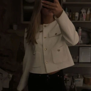 Vit kavaj från Zara - Säljer en stilren vit kavaj från Zara. Den har en croppad passform med långa ärmar och snygga guldknappar framtill. Perfekt för både vardag och fest! 🕊️✨ Aldrig använd. Nypris 600