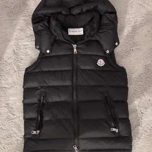Moncler väst - Moncler väst med avtagbar luva (man kan ta bort luvan) i strö XXS men den passar även S! Kan skicka fler bilder. Det är en k 0pia men märks inget. Superfiiin men ville ha en lite tightare så har aldrig använt den endast testad på bild!!
