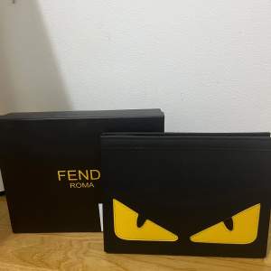 Säljer en supercool svart väska från Fendi med ikoniska gula ögon. Perfekt för att ge din outfit en edgy touch! Väskan är i syntetmaterial och har en dragkedja för säker förvaring. Kommer med originalförpackning. Perfekt för både vardag och fest!