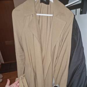 Säljer en snygg beige trenchcoat från Bik Bok i storlek S. Den har en klassisk design med bälte i midjan och långa ärmar. Perfekt för höst och vår när du vill se stilren ut. Jackan är i mycket bra skick och redo för nya äventyr!