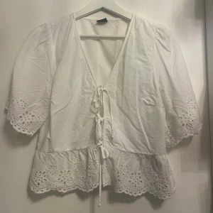 Vit blus - Säljer denna fina vita blus, använd 1 gång. Fin blus med knytning och volanger!