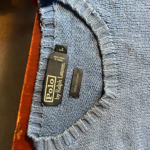 Blå stickad tröja från Polo Ralph Lauren - Säljer en snygg blå stickad tröja från Polo Ralph Lauren. Den är i storlek L och gjord av 100% bomull, vilket gör den superbekväm och perfekt för kyligare dagar. Tröjan har långa ärmar och en klassisk rund halsringning. Perfekt för både vardag och lite finare tillfällen!