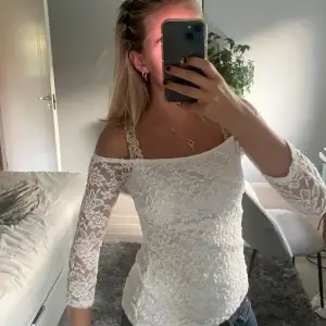 Säljer en superfin vit spetsblus med offshoulder-design. Den har långa ärmar och en tight passform som framhäver figuren. Perfekt för festliga tillfällen eller en utekväll. Blusen är i nyskick och ger en romantisk och elegant look.