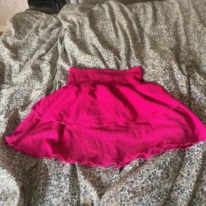 Rosa kjol från Gina Tricot - Säljer en superfin rosa kjol från Gina Tricot! Den har en smockad midja som ger en bekväm passform och volanger som ger en söt och lekfull look. Perfekt för sommardagar eller en festlig kväll. Kjolen är i bra skick och redo för nya äventyr! 💖