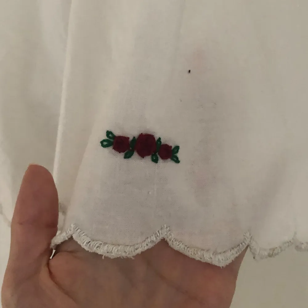 Säljer en söt vit kofta (typ) med trekvartsärm och en röd rosett vid halsen. Blusen har fina broderade blommor i rött och grönt vid ärmslutet och en vågig kant. Perfekt för en somrig look!. Jackor.