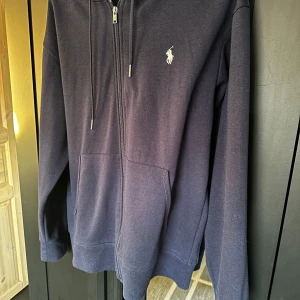 Mörkblå hoodie från Ralph Lauren - Säljer en snygg och stilren mörkblå hoodie från Ralph Lauren. Den passar dig som är runt omkring 180cm lång och har en hyfsat smal passform. 