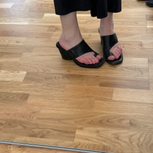 Svarta klackskor med krokodilmönster - Säljer ett par snygga svarta klackskor med en cool krokodilmönstrad yta. De har en öppen tå och en bred klack som ger bra stabilitet. Perfekta för en utekväll eller fest! 🖤