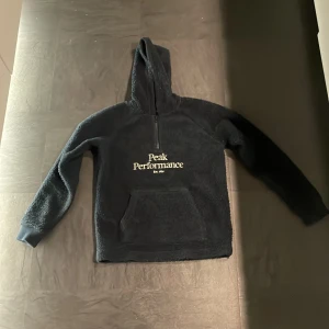 Mörkblå  fleece hoodie från Peak Performance - Säljer en mörkblå fleece hoodie från Peak Performance. Den har en dragkedja vid halsen och en stor ficka framtill. Perfekt för kyliga dagar med sin mjuka och varma känsla. Huvan ger extra skydd mot väder och vind. Köpt på Peak performance.