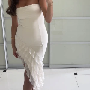 Vit axelbandslös klänning med volangdetaljer - Säljer min jättefina studentklänning med volanger nedtill. Superfin å sitter så bra på mig som vanligtvis är 36/S, skulle även passa en 34/xs. Jag är 170cm för referens!! 