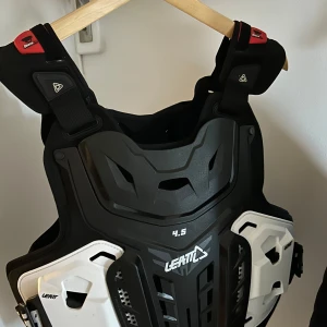 Svart skyddsväst från Leatt XXL - Säljer en robust svart skyddsväst från Leatt, modell 4.5. Västen har en cool design med vita detaljer och är perfekt för att ge extra skydd vid olika aktiviteter. Den är justerbar för en bekväm passform och har en modern look. Strl XXL