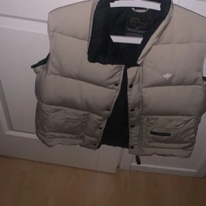 Pris kan diskuteras, meddela mig om prisförslag eller frågor😃 - Säljer en beige dunväst från Canada Goose. Västen har en quiltad design med knappar framtill och två praktiska fickor. Perfekt för kyligare dagar och ger en stilren look. Använd en gång, som ny från tidigt 2000- tal. Jag är 184 cm runt 88 kg och den sitter perfekt.