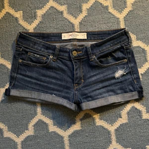 Lågmidjade jeansshorts från Abercrombie & Fitch - Snygga lågmidjade jeansshorts från Abercrombie & Fitch. De har coola slitna detaljer. Perfekta för sommardagar! Midja: 38cm rakt över. 
