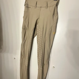 Beige ridbyxor - Snygga beige ridbyxor med helgripp och medel låg midja. Byxorna har en tight passform och är tillverkade i en blandning av polyester och spandex för extra stretch och komfort. Perfekta för ridning med praktiska detaljer som knappar och fickor, använda 3 gånger på tävling men legat i garderoben sen dess🥰