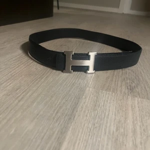 Svart bälte med silverfärgat H-spänne - Stilrent svart bälte med ett iögonfallande silverfärgat H-spänne. Perfekt för att ge en elegant touch till din  outfit.