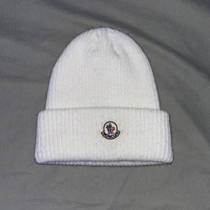 Vit ribbad mössa från Moncler - Snygg vit ribbad mössa från Moncler med broderad logotyp framtill. Perfekt för att hålla värmen under kyliga dagar. Stilren design som passar till det mesta.