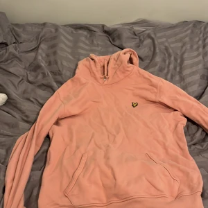 Rosa hoodie från Lyle & Scott - Säljer en snygg rosa hoodie från Lyle & Scott. Den har en klassisk design med en liten logga på bröstet och en praktisk ficka framtill. Perfekt för en avslappnad stil.