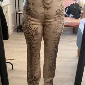 Beige mönstrade byxor - Snygga beige byxor med ett unikt mönster. De är högmidjade och har en straight passform som ger en stilren look.