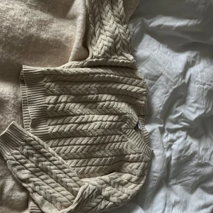 Beige stickad kofta från Lindex - Säljer en mysig beige stickad kofta från Lindex med flätmönster. Koftan har långa ärmar och ribbade muddar vid ärmslut och nederkant. Perfekt för kyliga dagar! Jag änvänder den på julen och när det är kalt på sommaren. Säljer den eftersom inte användning 