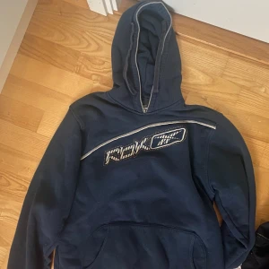 Mörkblå hoodie från Reebok - Säljer en mörkblå hoodie från Reebok med en stor logga på bröstet. Hoodien har en klassisk design med en stor ficka framtill och en bekväm huva med snörning. Perfekt för en avslappnad stil.