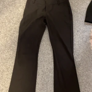 Svarta kostymbyxor - Snygga svarta kostymbyxor med dragkedja och knappar. Perfekta för en stilren look. Byxorna har en klassisk passform och är tillverkade i ett bekvämt material. Knappen saknas