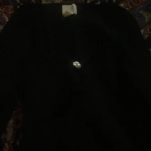 Svart tröja med knappdetalj - Säljer en stilren svart tröja med en unik knappdetalj framtill. Perfekt för en minimalistisk look. Tröjan har en enkel design som gör den lätt att matcha med olika outfits.